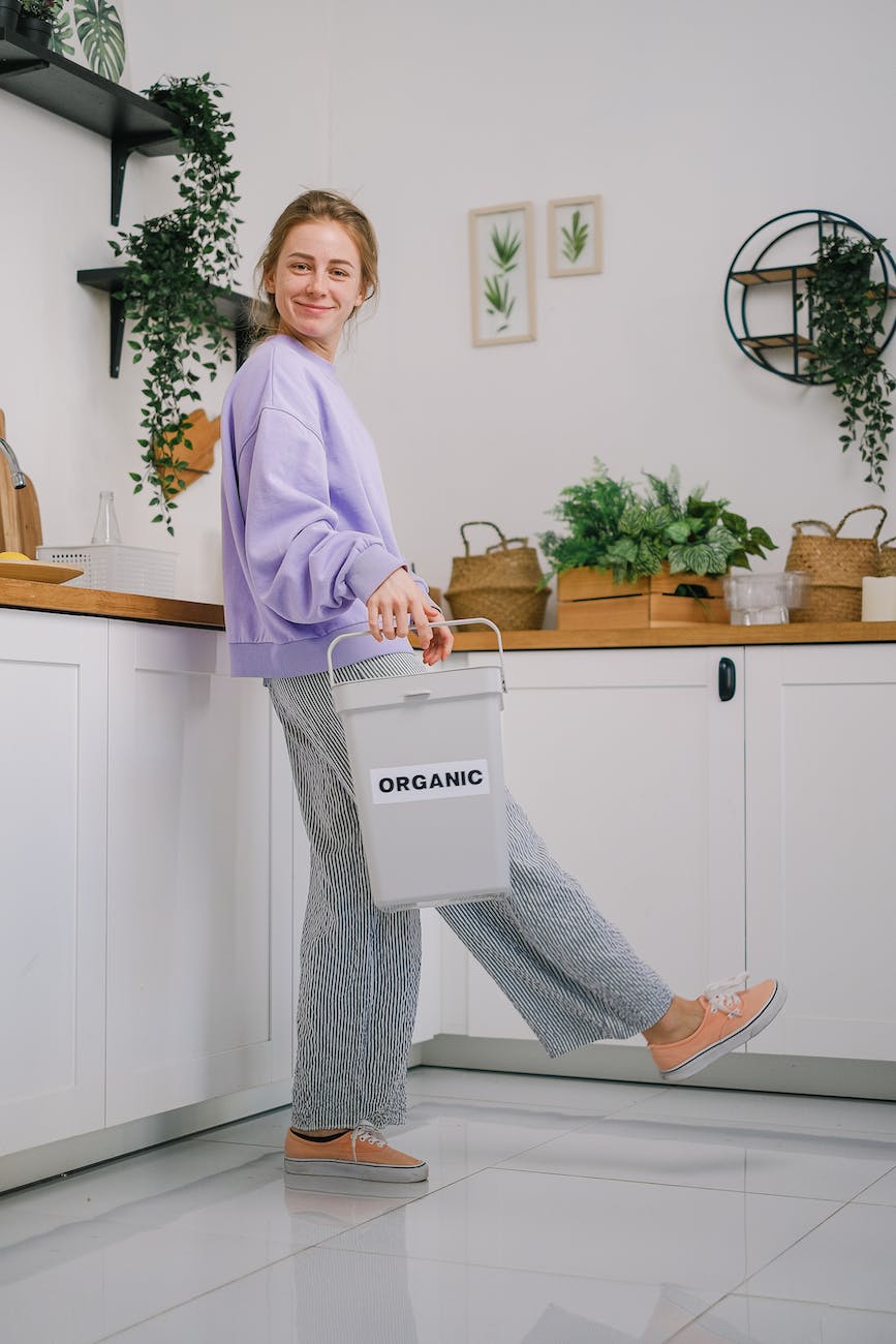 smiling female standing with container with organic trash in kitchen