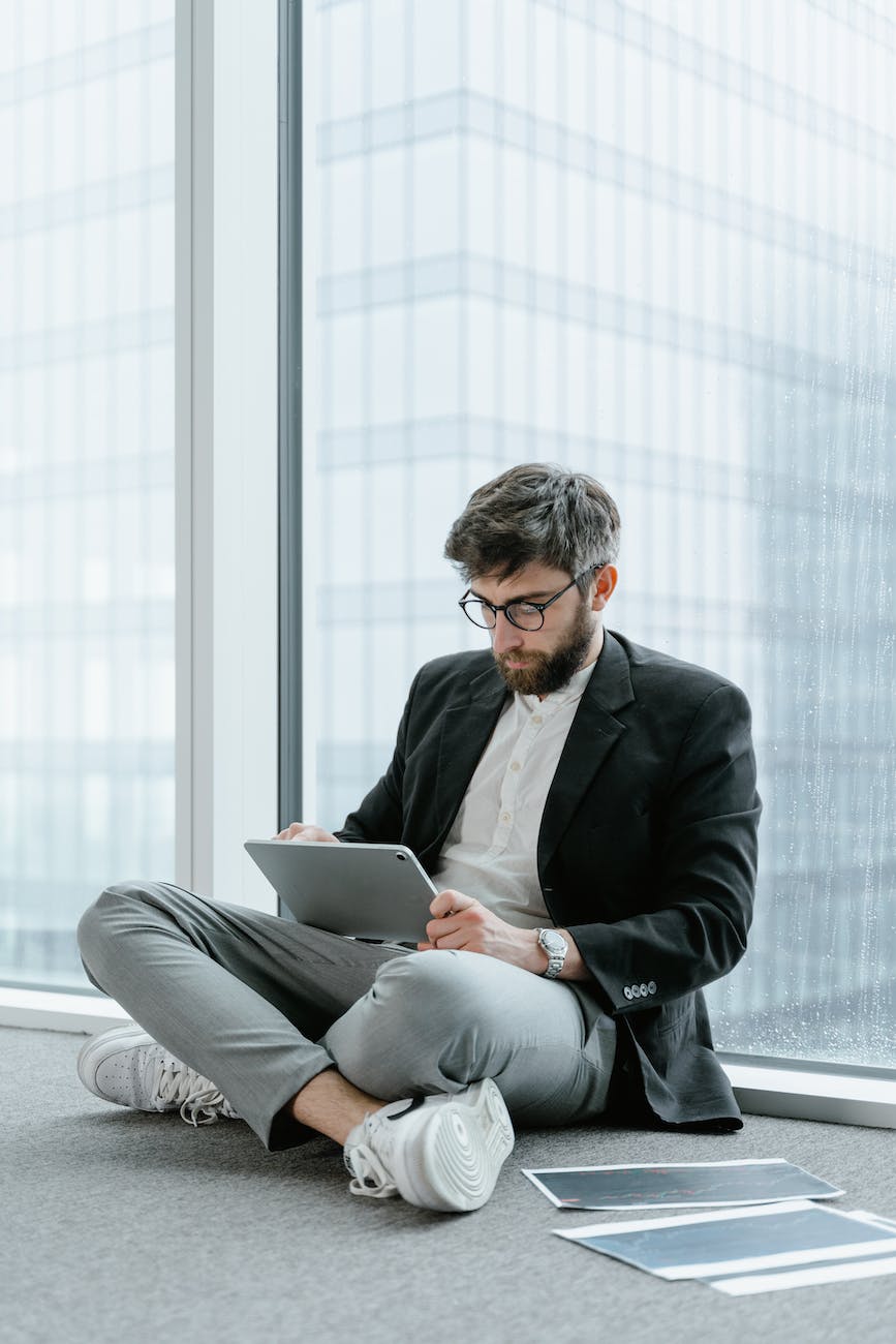 bearded man in black suit jacket sitting on floor using digital tablet